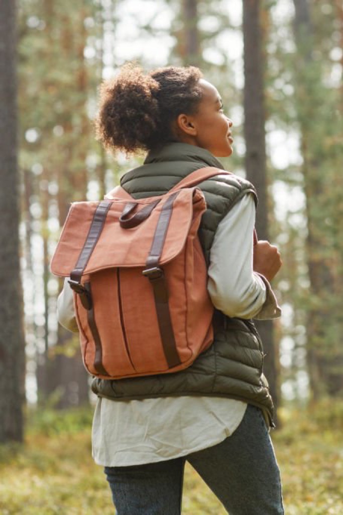 Young woman with a backpack looking ahead as she walks through a sunlit forest